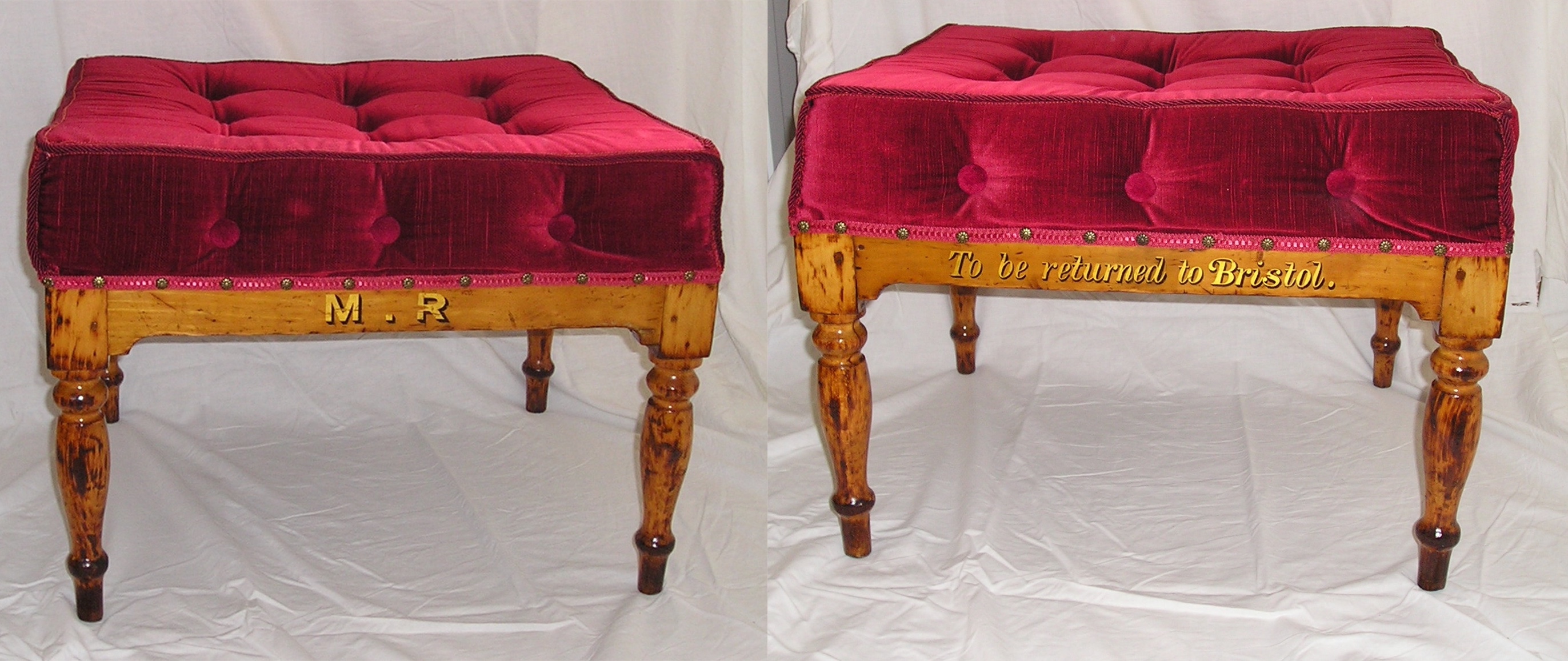 A low, highly varnished wooden stool with deep red upholstery. The front and back are shown side-by-side. The front reads, in gold lettering, 'M.R' while the back reads ' To be returned to Bristol'. 
