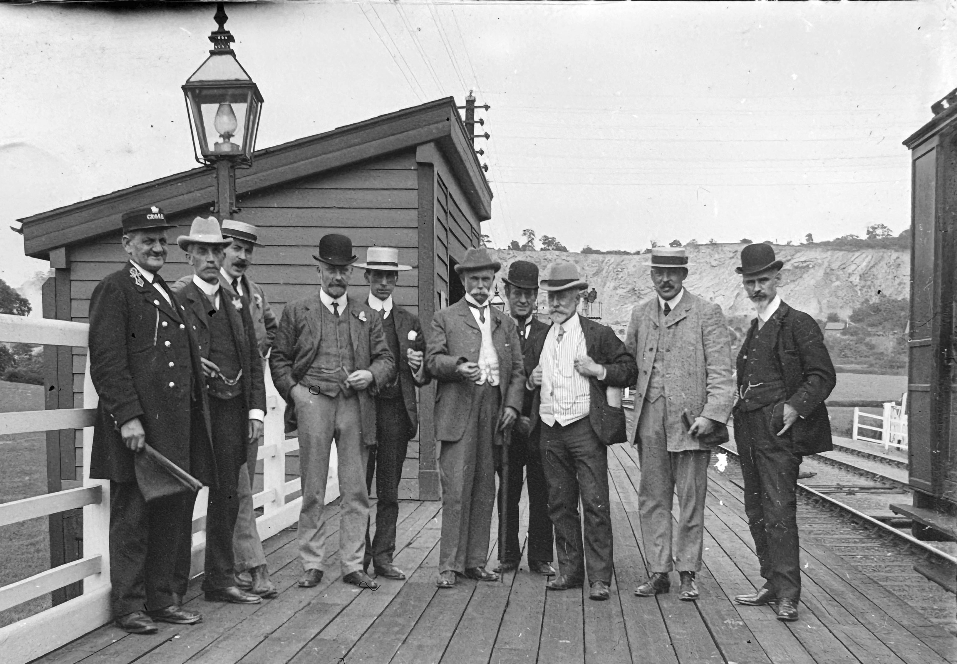 A group of ten men, including a Midland Railway Guard on the left, standing on a wooden station platform, posing for the photographer.