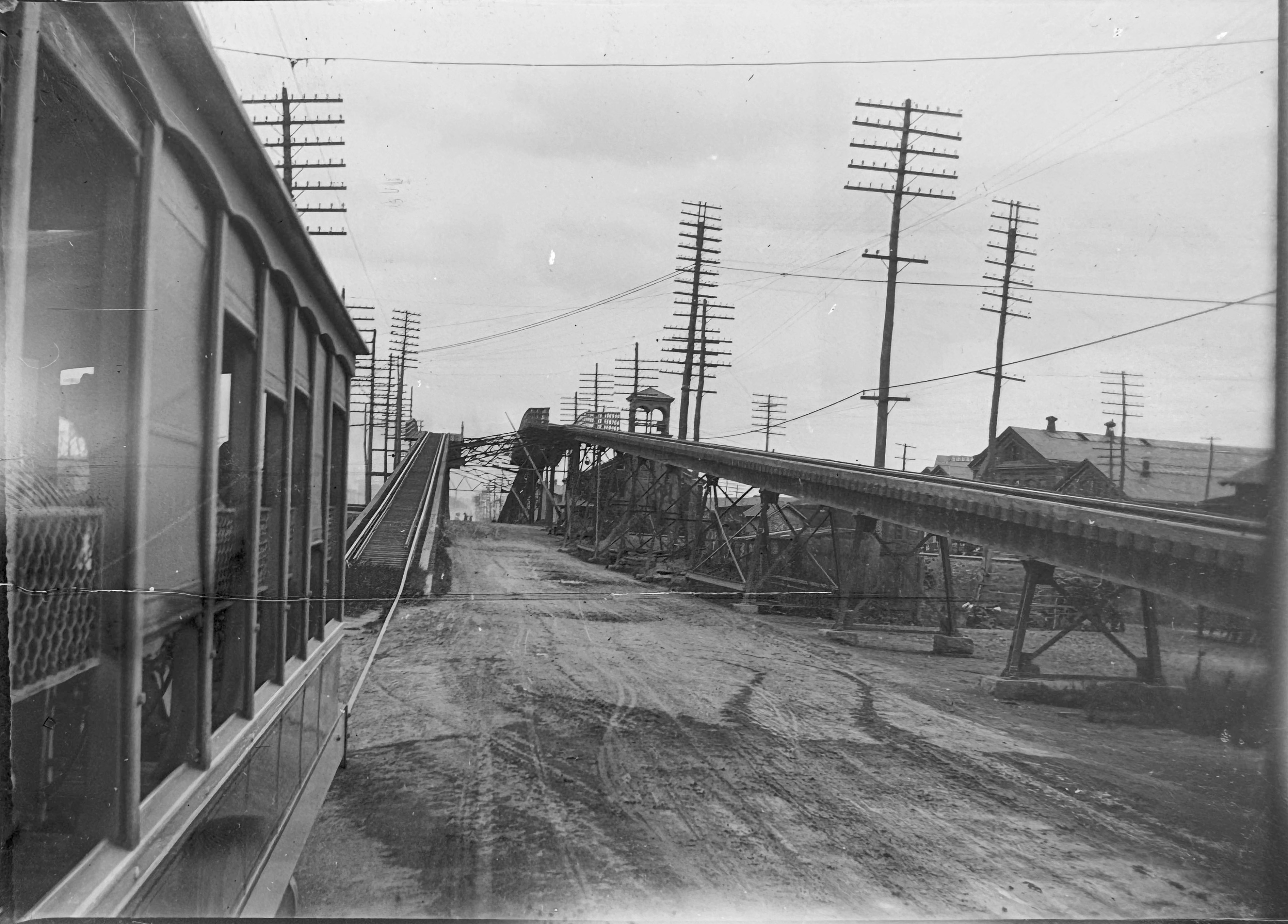 A view taken out of the window of an American street car that has just descended from a very rickety looking bridge carrying the rails across a road intersection