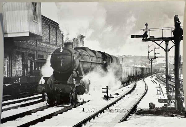 Stanier 8F arrives at the same station as the image abover in the opiste direction hauling a mineral train in a snow covered scene.