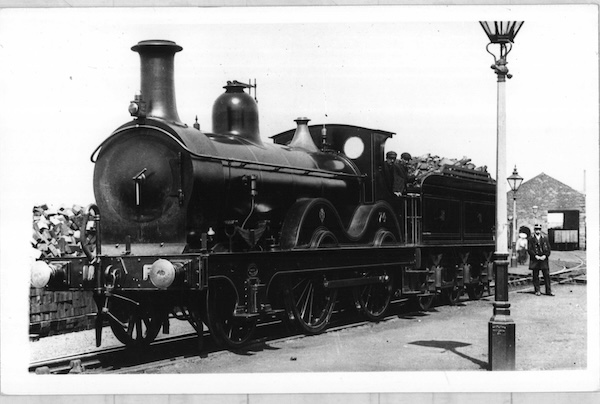 Midland Railway 2-4-0 No.74 stands in a small goods yard with a brick goods shed in the background. The crew and what looks like the Station Master are posing for the photographer.