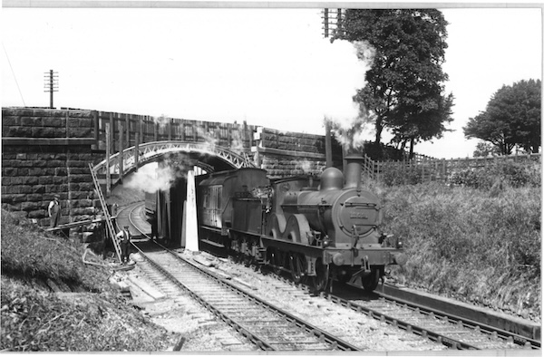 Photograph of workmen looking on as Midland Railway 1400 Class 2-4-0 No. 209 heads an express passenger train under a bridge that is supported by temporary timbers while it is being rebuilt.