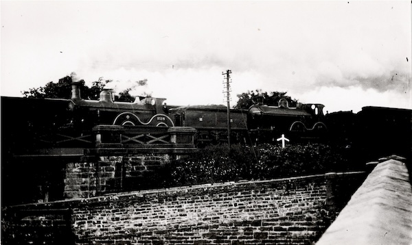 Photograph of a double headed Down Express  at an unidentified location. The photographer is standing on a bridge crossing what may be a canal, which then passes under the railway.