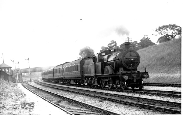 Ex-Midland Railway 4-4-0 No.711 in its LMS guise heads a passenger train past a Midland Railway signal box on a four-track section of line. Significantly, it is on the third line away from the photographer, indicating a configuration where Goods Line are on the outside of the formation.