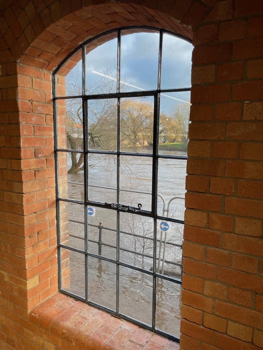 Viewed through an arched window, the River Derwent outside is in flood