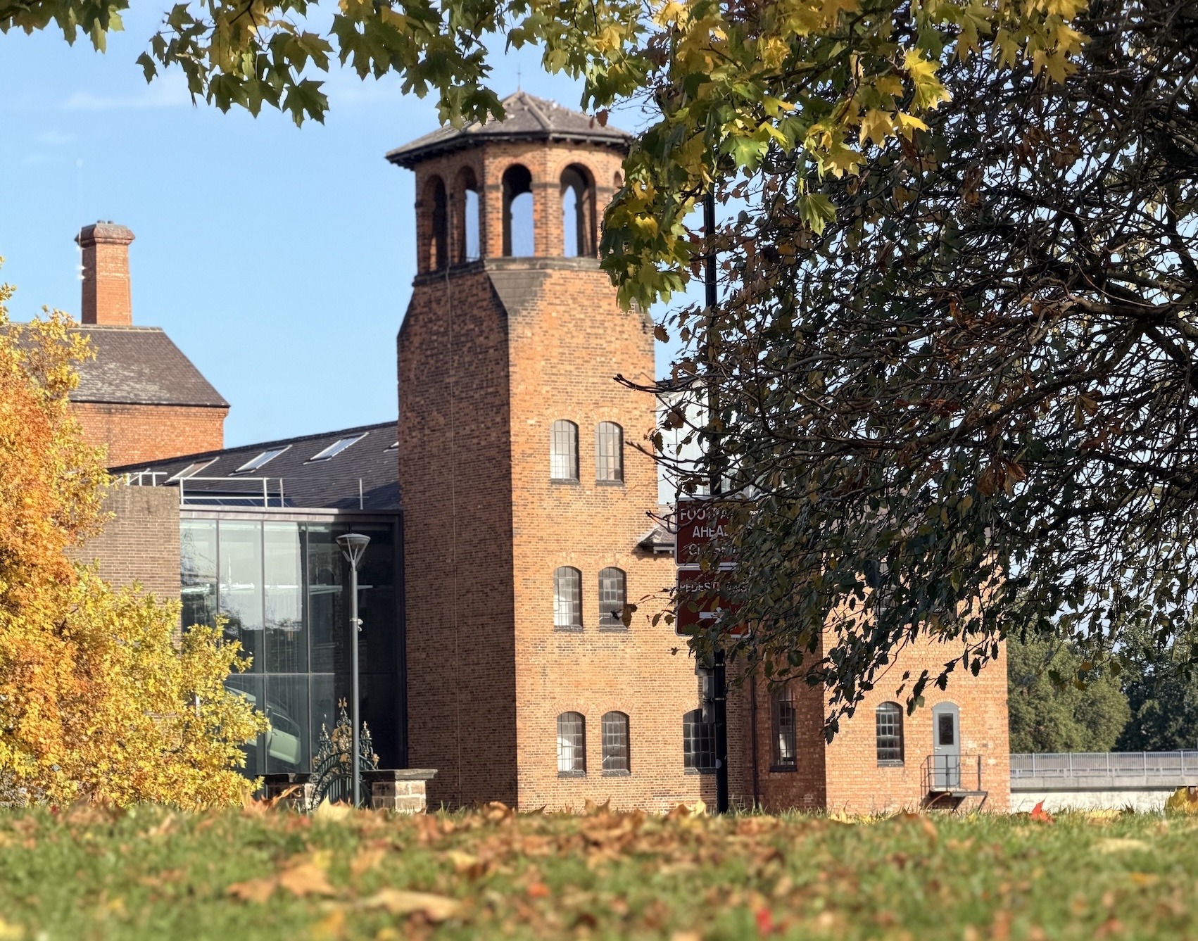A mid-distance view of Derby's Silk Mill across Cathedral Green, framed by autumnal colours.