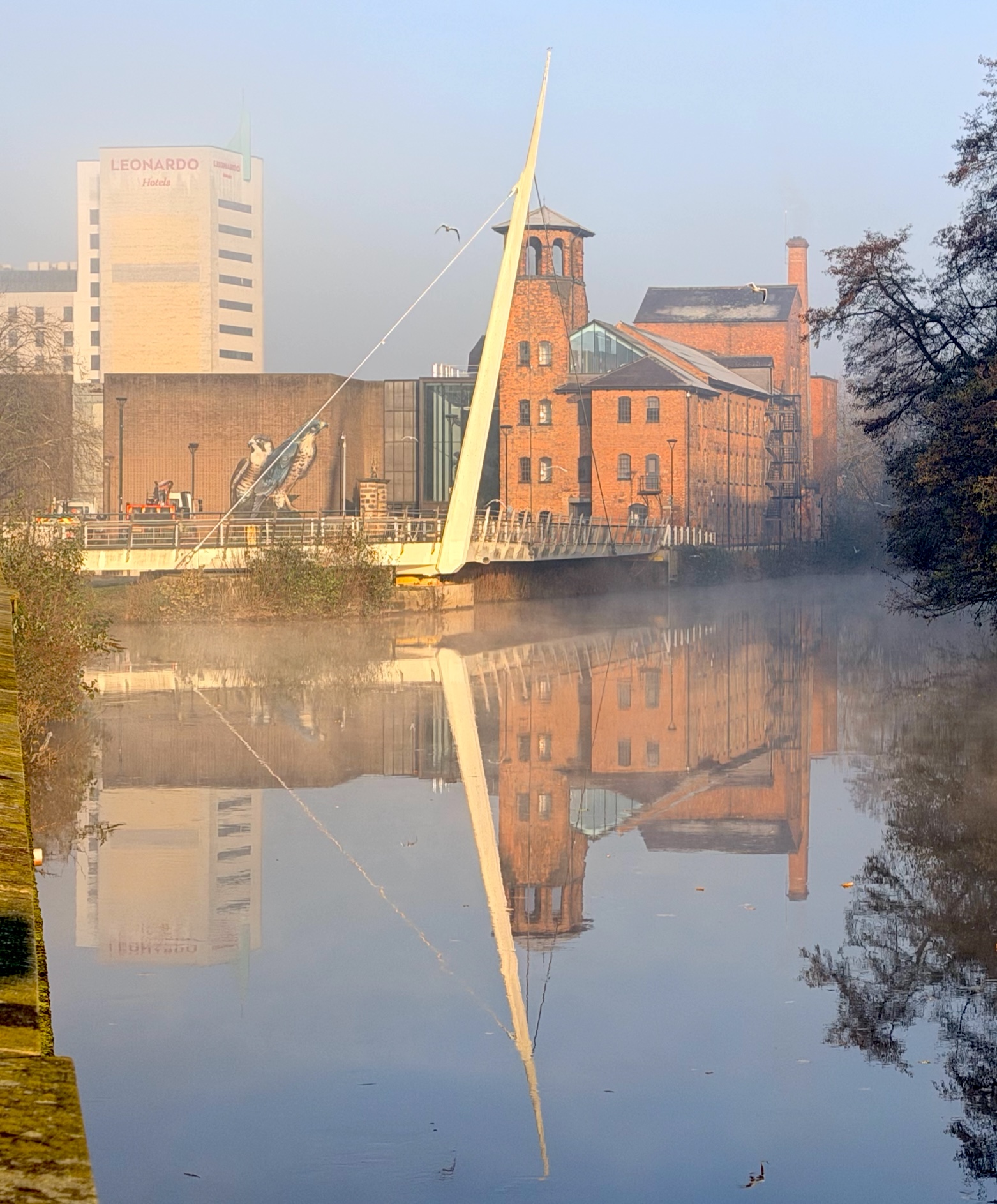 A view of the Silk Mill at Derby, illuminated by the low winter sun, viewed on the distance along the River Derwent through the mist of a December morning.