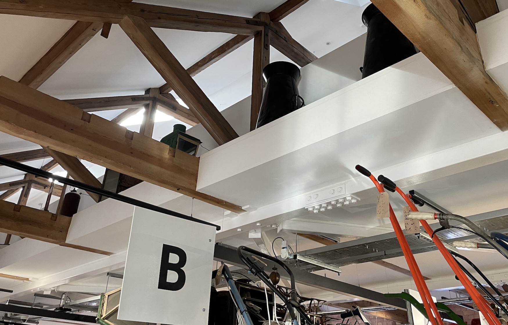 Looking up at the rafters we see a mezzanine floor above us with various items located on the edge it forms, including some milk churns