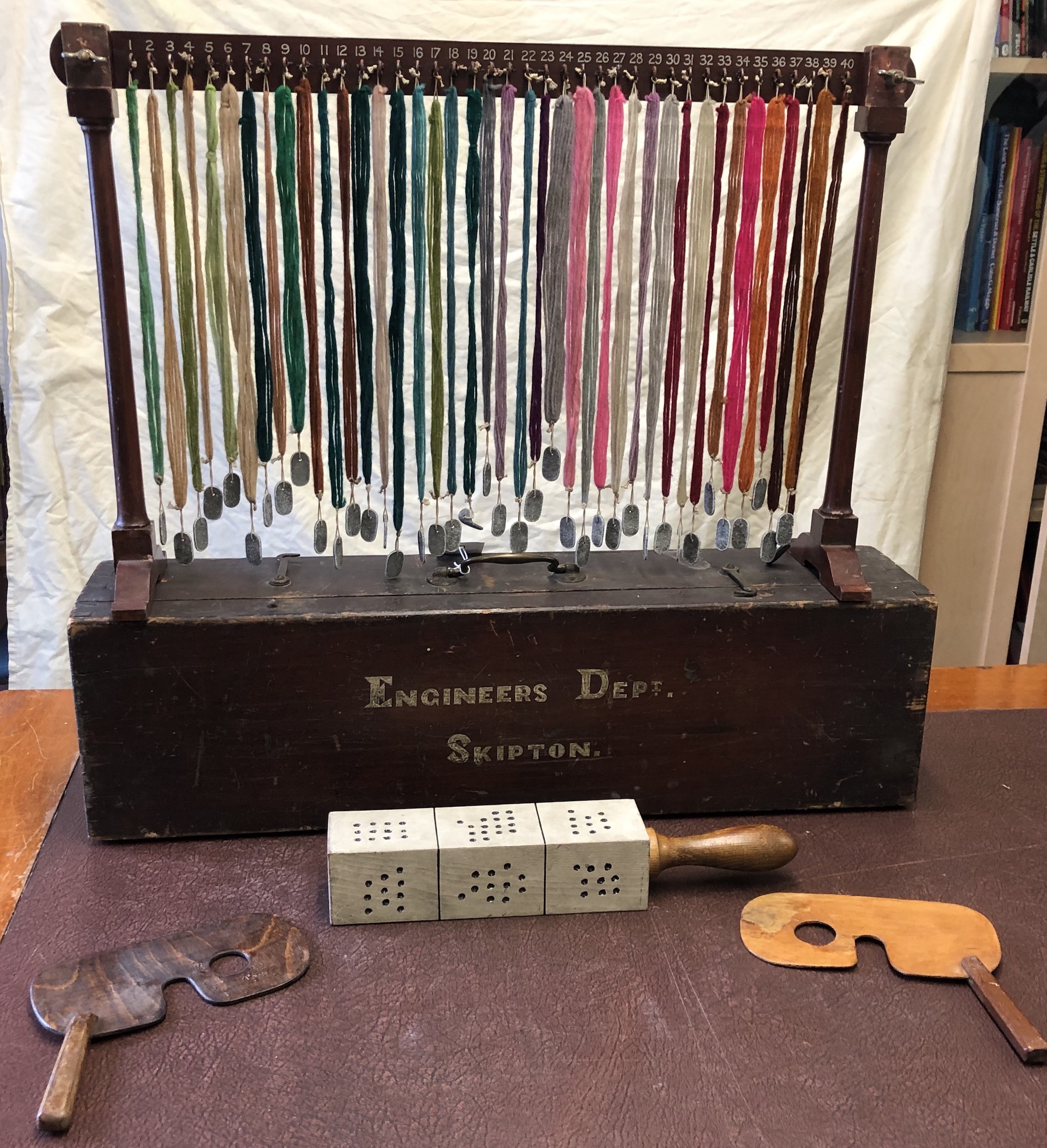 Eyesight tester formed of a frame from which multiple weighted strands of coloured wool are suspended, along with eye covers and a block with multiple dots for eyesight testing. All contained within a case marked ‘Engineers Dept. Skipton’. 20in high when erected.