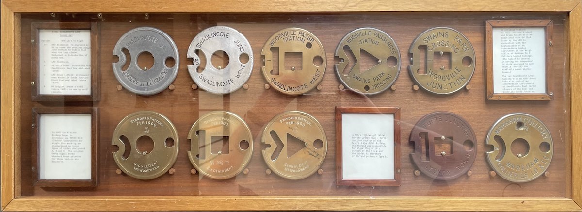 A display case containing ten discs of about five inches diameter made of either brass or silver alloy. Each has various notches cut out of them and are inscribed with the name of the signal boxes they relate to; Swadlincote Junction, Swadlincote West, Woodville Passenger Station, Woodville Goods Junction or Swains Park.