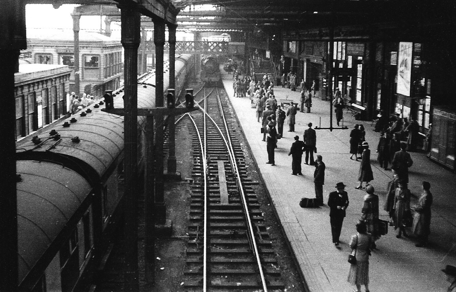 A photogrpah illustrating the view south along Platform 1 of Derby station in 1952 from the Locomotive Works footbridge. The colour light electric signals we ar elooking at can be seen mounted on wooden posts, with the metal bracket they were once on hangs from the roof over Platform 1.